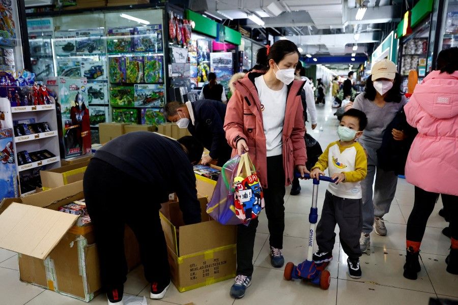 A woman and a child walk past workers sorting toys at a shopping mall in Beijing, China, 11 January 2023. (Tingshu Wang/Reuters)