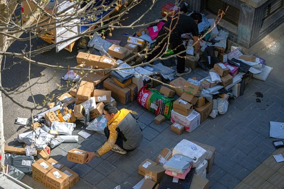 A delivery worker sorts packages on the side of a road in Beijing, China, on 28 April 2025. (Na Bian/Bloomberg)