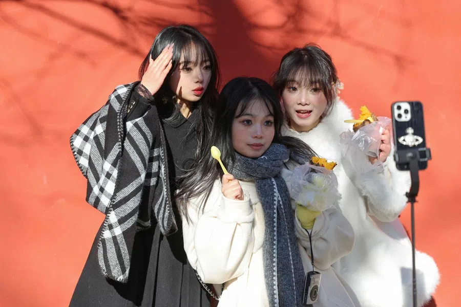 Chinese women holding sweet potato snacks pose for pictures on a street in Beijing on 2 December 2025. (Ludovic Marin/AFP)