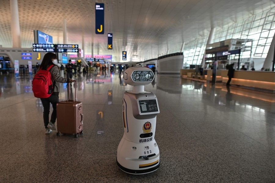 In this file photo taken on 8 April 2020 an airport police robot is seen while a passenger (L) wearing a face mask walks at the Tianhe Airport after it was reopened today, in Wuhan in China's central Hubei province. (Hector Retamal/AFP)