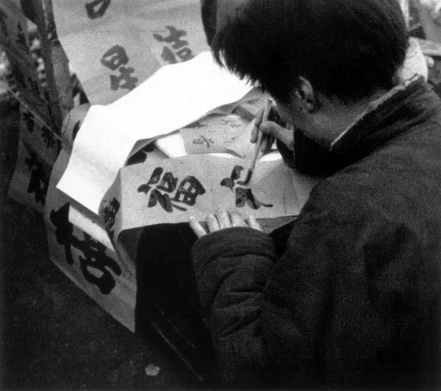 A vendor writes the Chinese character 福 (good fortune). New year wishes are usually either couplets (对联) or single words. For the latter, the characters 福 and 春 (spring) are the most common. These wishes are put up on the door or in various places around the home.