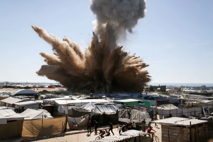 People run for cover as a plume of smoke rises above tents at a camp for displaced Palestinians in northern Khan Yunis in the southern Gaza Strip, during an Israeli strike on 19 April 2025.