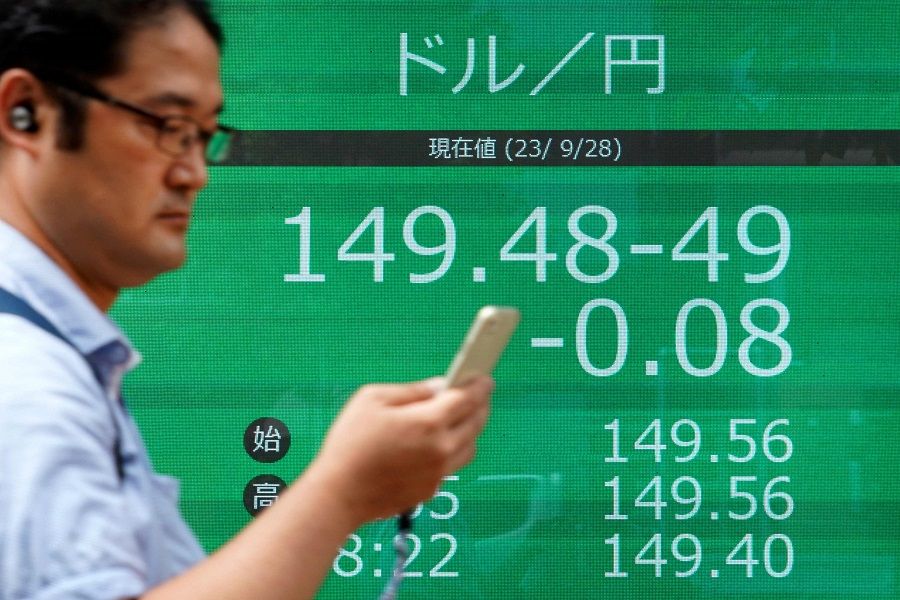 A man walks in front of an electronic board showing the rate of the Japanese yen versus the US dollar along a street in Tokyo on 28 September 2023. (Kazuhiro Nogi/AFP)
