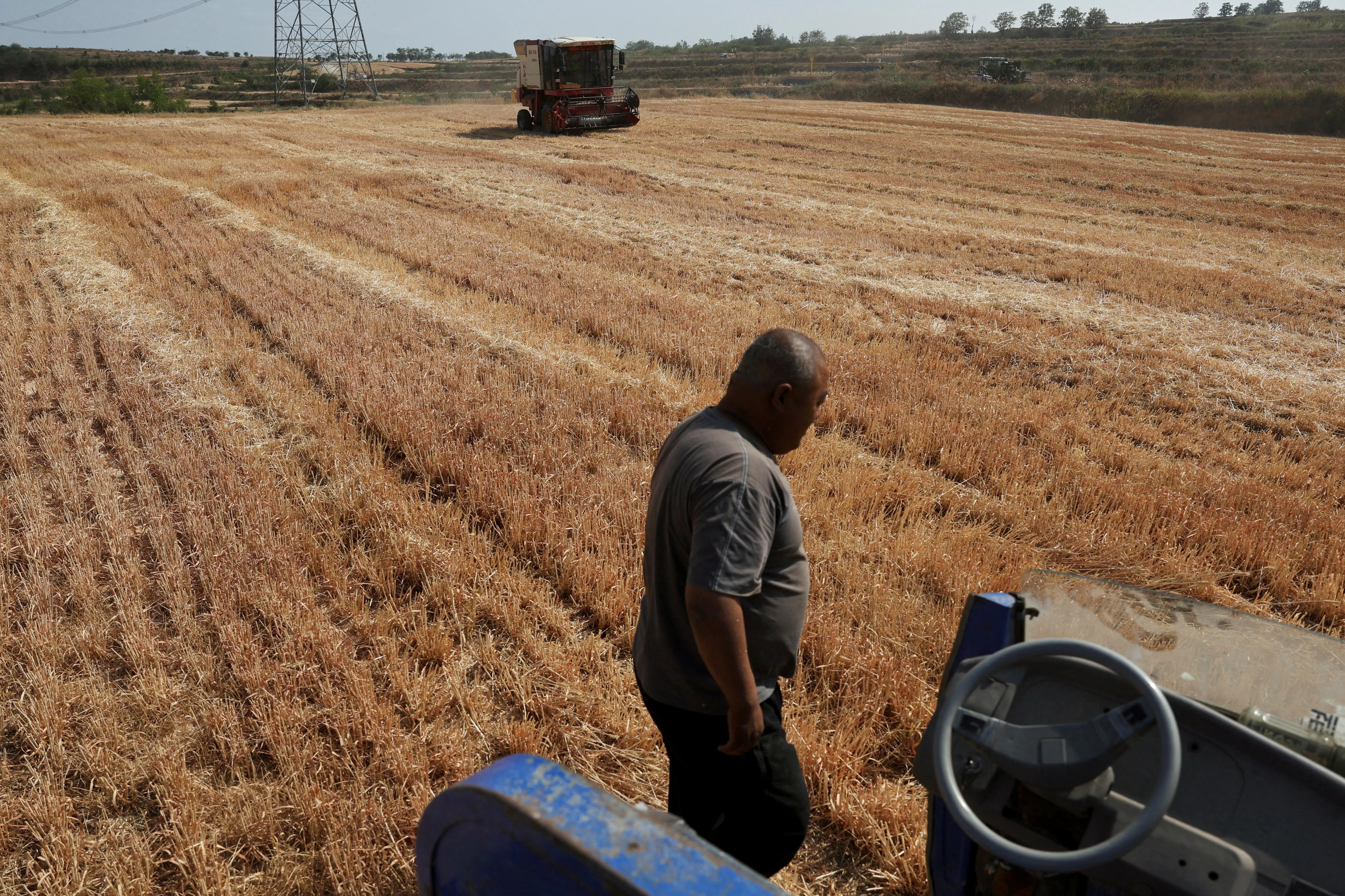 A farm worker waits for a combine harvester working on a wheat field at Yongshou county in Xianyang, Shaanxi province, China, on 29 May 2025.