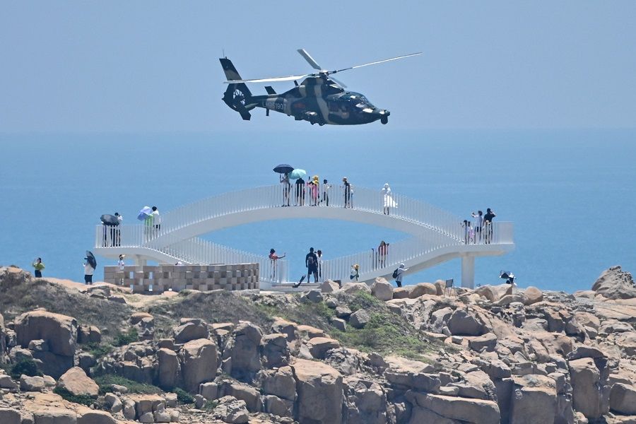 People look on as a Chinese military helicopter flies past Pingtan island, one of mainland China's closest points from Taiwan, in Fujian province, on 4 August 2022, ahead of massive military drills off Taiwan following US House Speaker Nancy Pelosi's visit to the self-ruled island. (Hector Retamal/AFP)