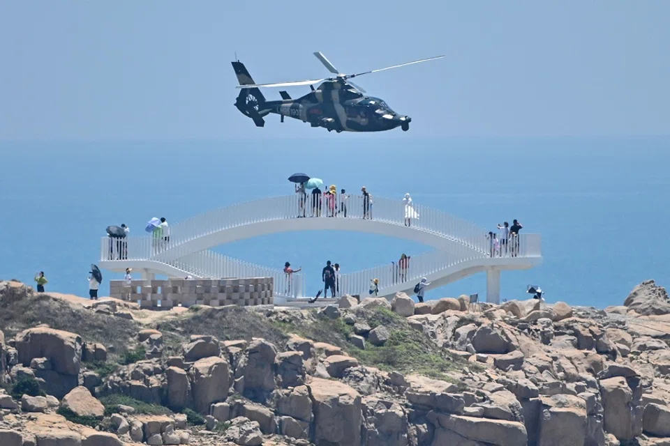 People look on as a Chinese military helicopter flies past Pingtan island, one of mainland China's closest points from Taiwan, in Fujian province, on 4 August 2022, ahead of massive military drills off Taiwan following US House Speaker Nancy Pelosi's visit to the self-ruled island. (Hector Retamal/AFP)