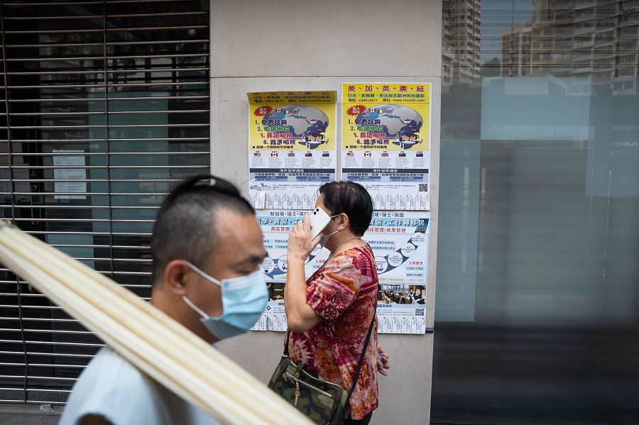 People walk past advertisements for immigration and studying abroad in Hong Kong's To Kwa Wan area on 11 September 2022. (Bertha Wang/AFP)