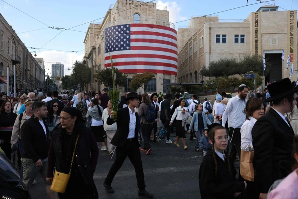 Israelis walk past a US flag in the heart of Jerusalem on 12 October 2025. (Ahmad Gharabli/AFP)