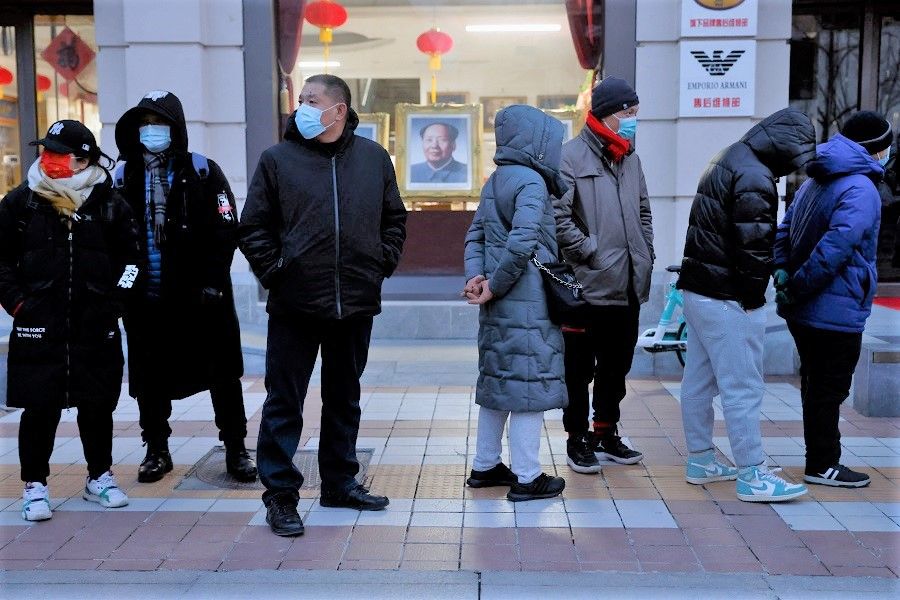 People wearing face masks stand in front of a painting of late Chinese chairman Mao Zedong, while waiting in line to enter a flagship merchandise store for the Beijing 2022 Winter Olympics before it opens, on Wangfujing Street in Beijing, China, 9 February 2022. (Carlos Garcia Rawlins/Reuters)