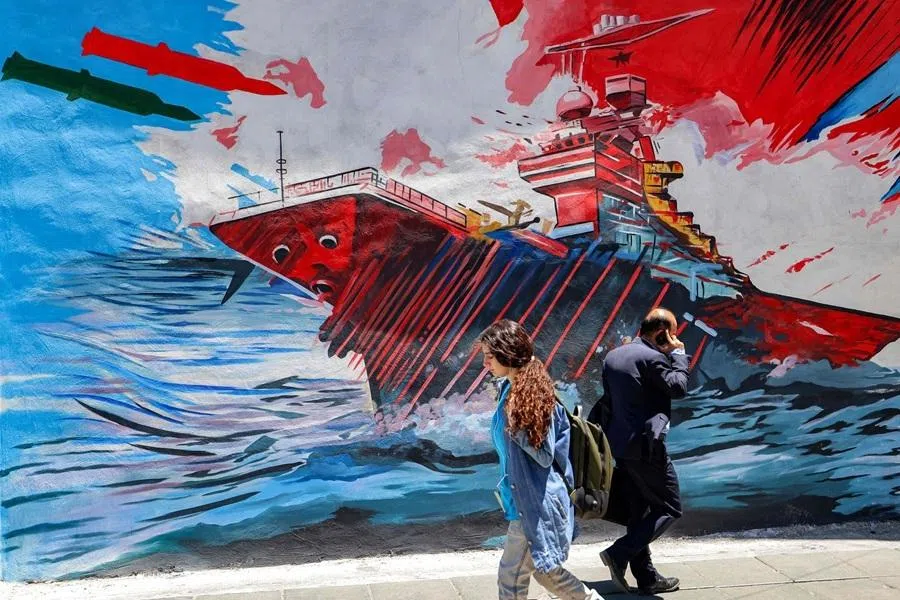 People walk past an anti-US and anti-Israel mural depicting missiles hitting an aircraft carrier in Tehran on 26 May 2026.