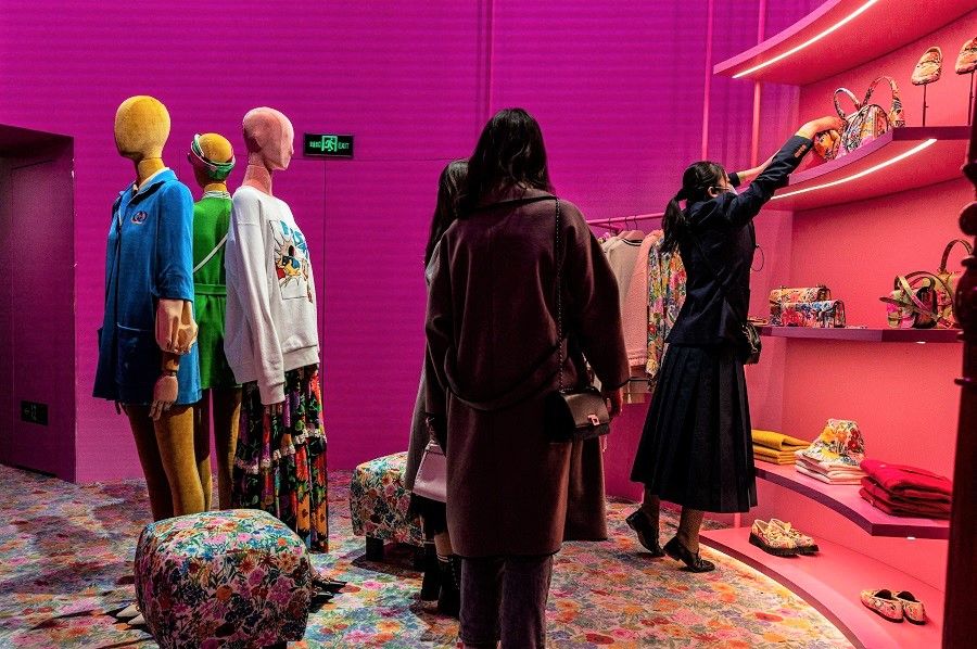 People shop inside a Gucci shop as an employee (right) grabs an item in Beijing, China on 13 April 2021. (Nicolas Asfouri/AFP)