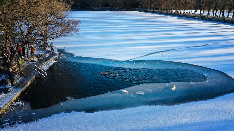 This aerial photo taken on 3 December 2022 shows a winter swimming enthusiast swimming in a partly frozen lake after snowfall in Shenyang, Liaoning province, China. (AFP)