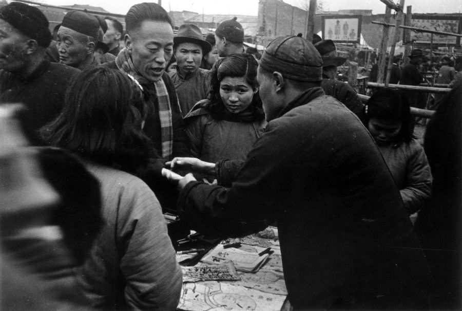 A seller of old books bargains with a customer at the Confucius Temple lantern fair. There are stalls selling old goods at the Confucius Temple fair, including some valuable antique and old editions.