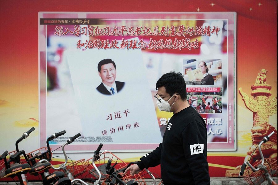 In this file photo taken on 12 March 2018, a man walks past a poster showing Chinese President Xi Jinping in Beijing, China. (Nicolas Asfouri/AFP)