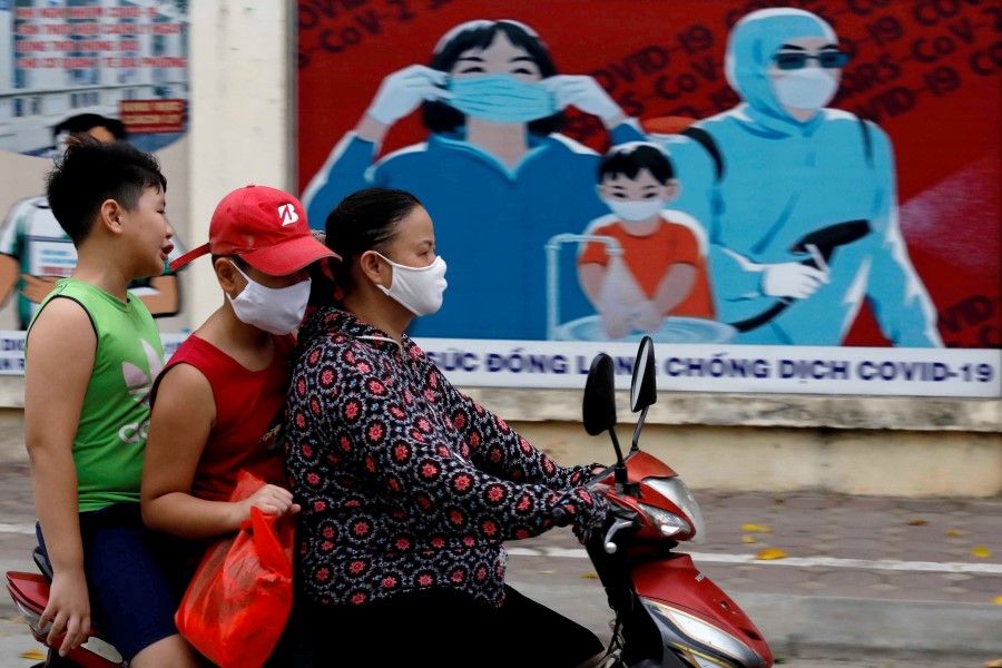 A woman wears a protective mask as she drives past a banner promoting prevention against the coronavirus disease (COVID-19) in Hanoi, Vietnam, 31 July 2020. (Kham/REUTERS)