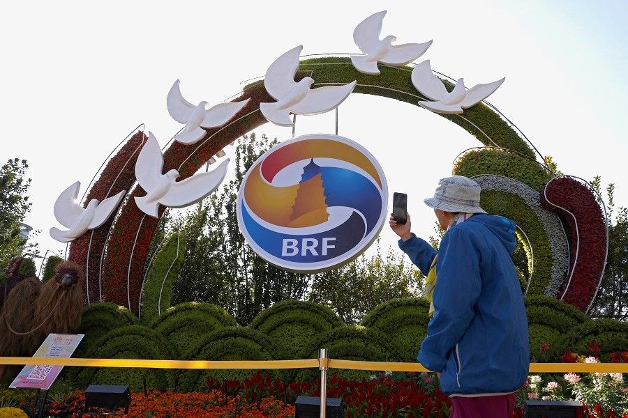 A person uses a phone in front of an installation featuring the logo of the third Belt and Road Forum, in Beijing, China, on 16 October 2023. (Tingshu Wang/Reuters)