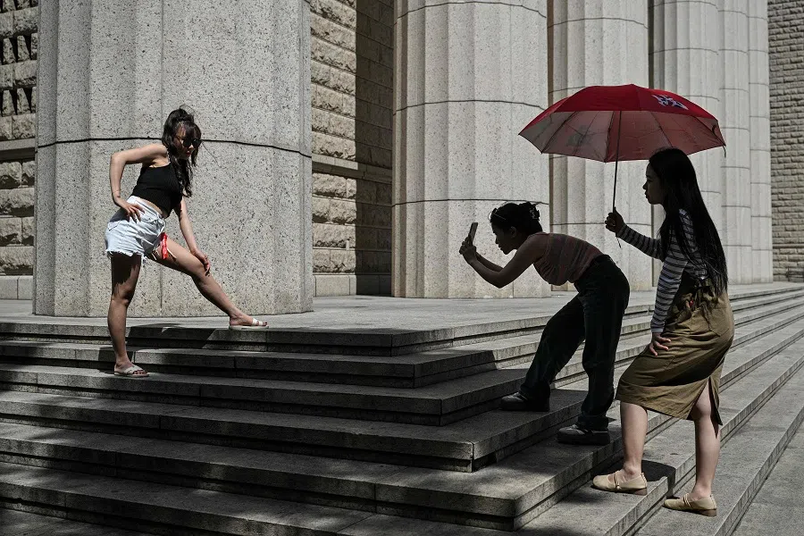 A woman poses for pictures next to a building at the financial district of Lujiazui in Shanghai on 23 September 2024. (Hector Retamal/AFP)