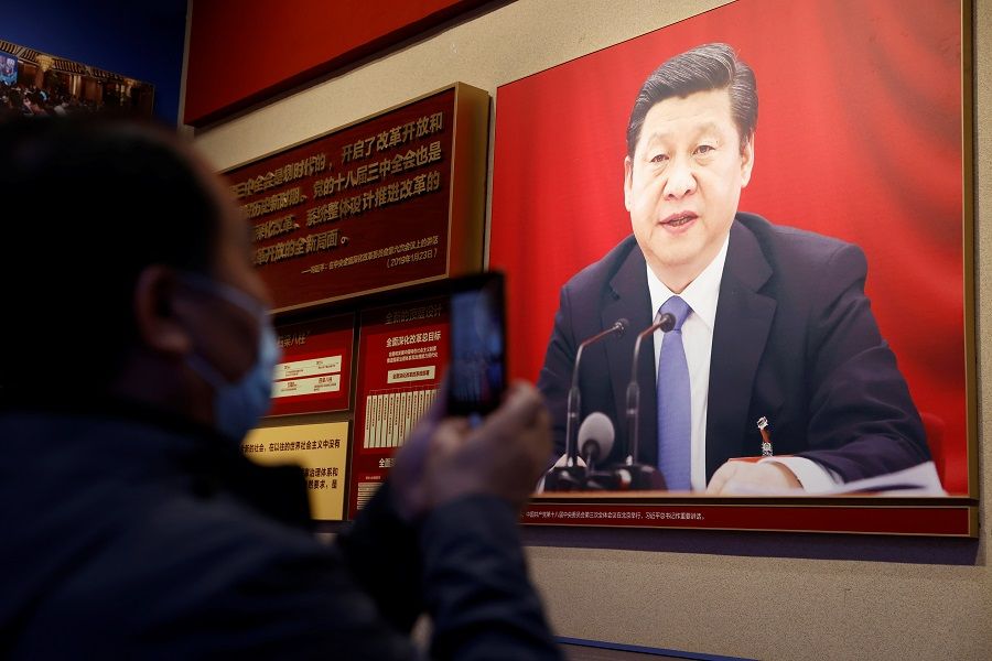 A man holds a mobile phone in front of an image of Chinese President Xi Jinping displayed at the Museum of the Communist Party of China in Beijing, China, 11 November 2021. (Carlos Garcia Rawlins/Reuters)