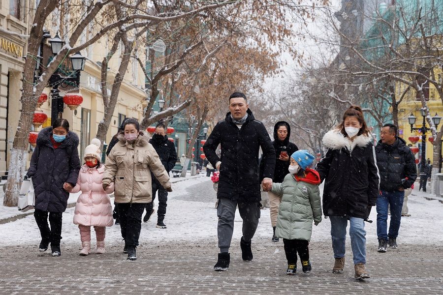 People walk with children on a street in Harbin, Heilongjiang province, China, 10 February 2023. (Thomas Peter/Reuters)