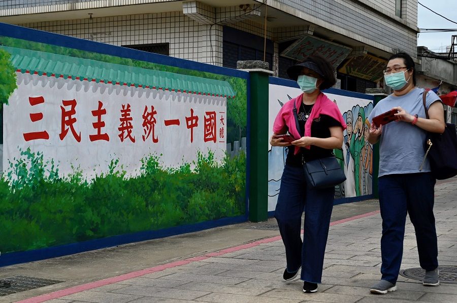 This photo taken on 21 October 2020 shows tourists passing a wall with a slogan that says "Grand Alliance for China's Reunification under the Three Principles of the People", on Taiwan's Kinmen islands. (Sam Yeh/AFP)