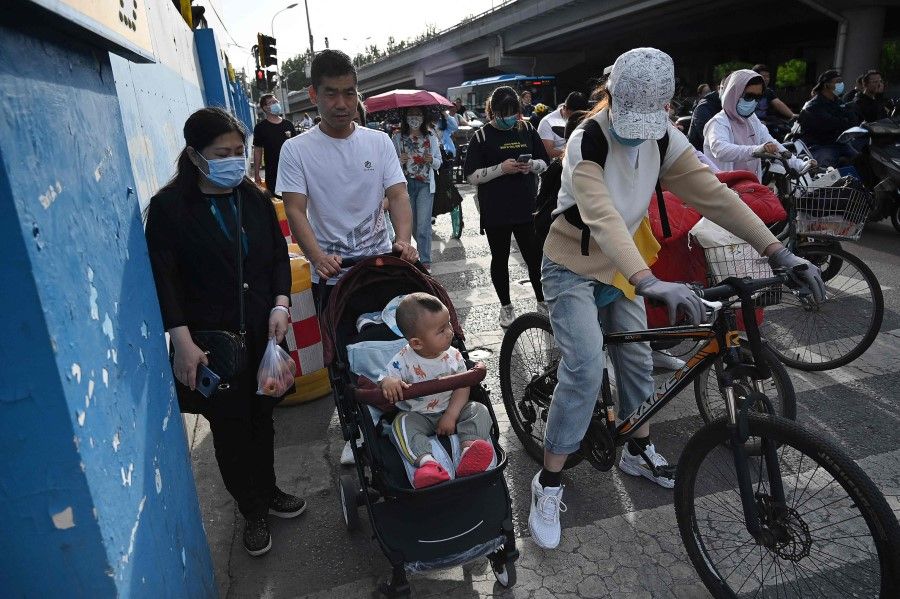 A couple pushes their child in a stroller between bicycles at a busy intersection in Beijing on 2 June 2021. (Greg Baker/AFP)