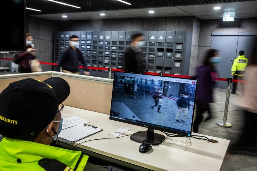 A security guard (bottom) monitors a temperature checkpoint as people arrive at the entrance to a government office building in Hong Kong on March 2, 2020. Hong Kong's civil servants returned to their offices after having worked from home since the Lunar New Year holiday in January. (Isaac Lawrence/AFP)