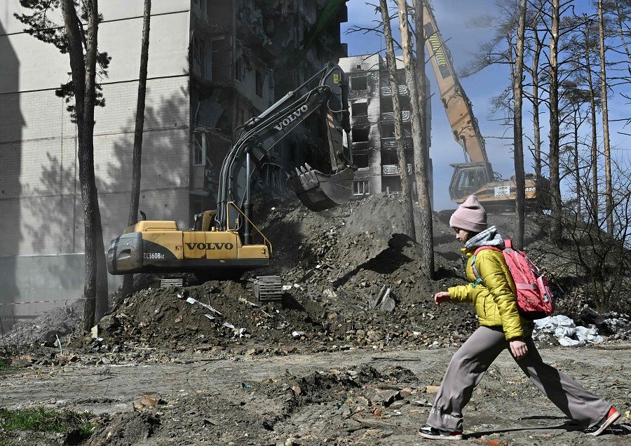 A girl walks past a heavily damaged residential building as workers dismantle it in the town of Irpin, Ukraine, on 21 April 2023, amid the Russian invasion of Ukraine. (Genya Savilov/AFP)