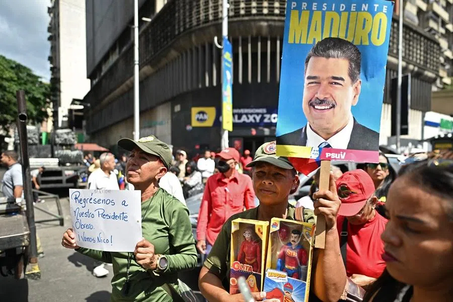 A supporter of ousted Venezuelan President Nicolas Maduro holds a poster of him and toys of him and his wife, Cilia Flores, as another one holds a sign reading "Give us back our worker President. Go Nico!" during a demonstration in Caracas on 4 January 2026, a day after he was captured in a US strike.