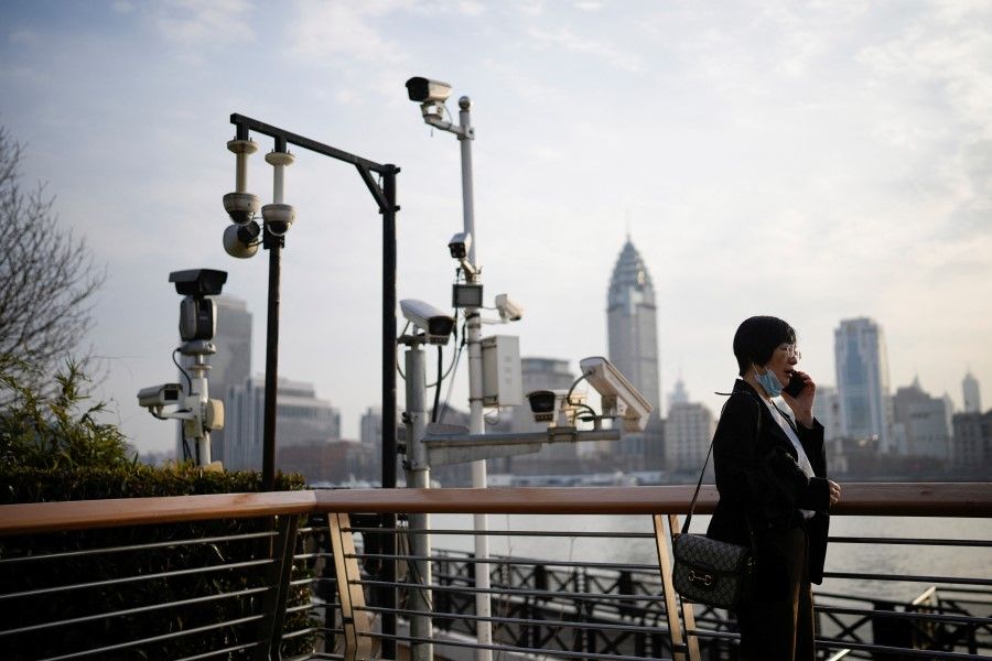 A woman talks on a phone under surveillance cameras on a riverside in Shanghai, China, 7 March 2023. (Aly Song/Reuters)