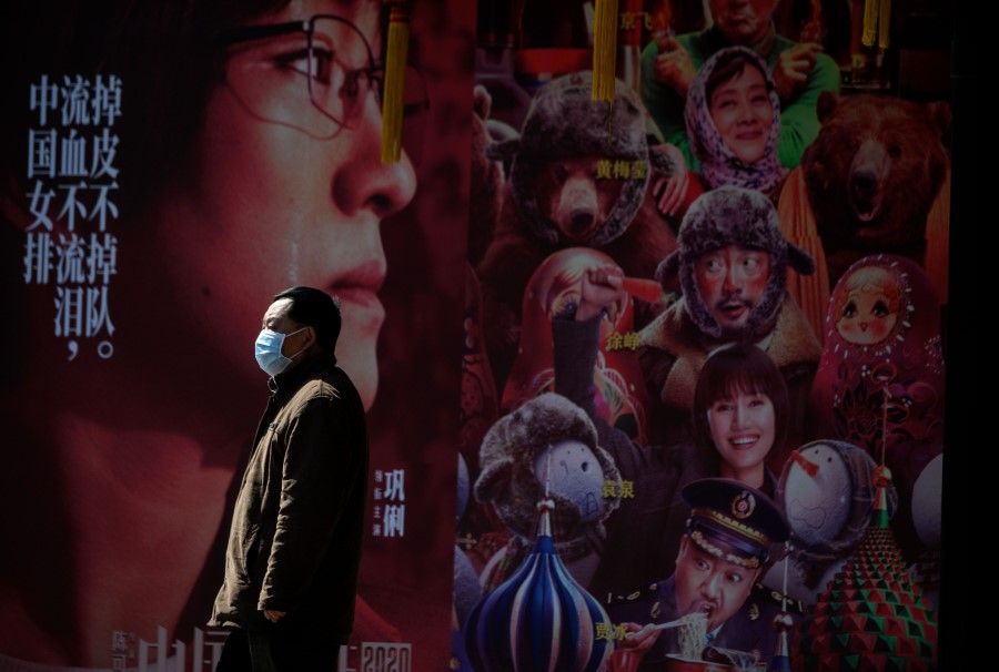 A man wearing a protective facemask stands in front of a movie poster in Shanghai. - China on February 19, 2020 ordered three reporters from American newspaper the Wall Street Journal to leave the country over what Beijing deemed a racist headline, in one of the harshest moves against foreign media in years. (Noel Celis/AFP)