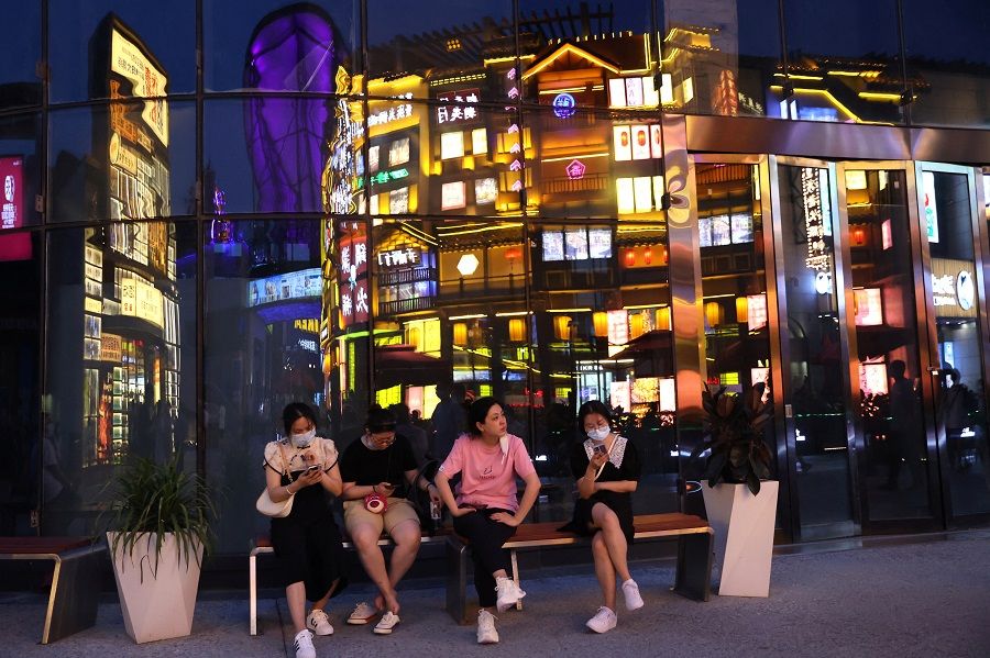 People sit near a building reflecting a restaurant, at a shopping area in Beijing, China, 25 July 2022. (Tingshu Wang/Reuters)