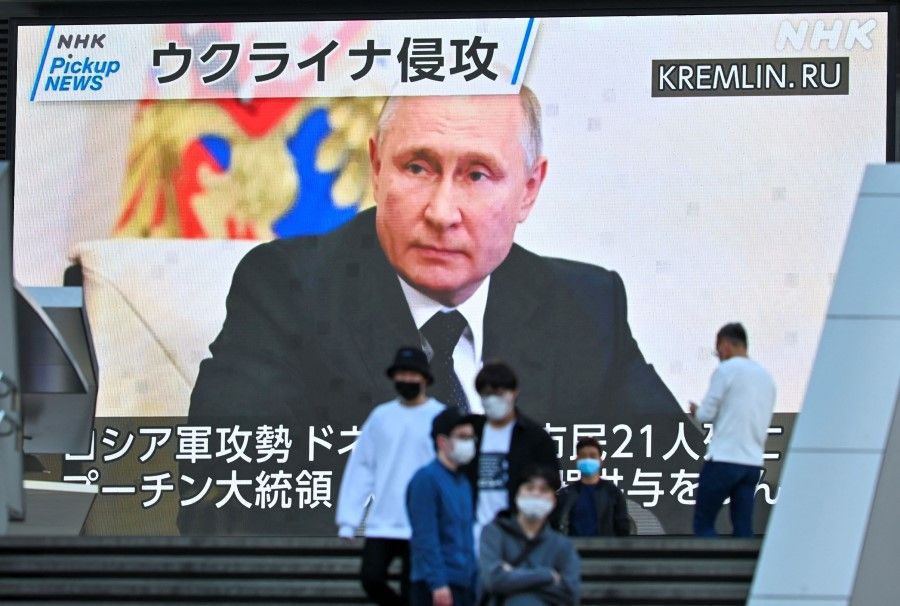 Pedestrians walk past a screen displaying Russian President Vladimir Putin during a news broadcast about Russia's invasion of Ukraine, in the Akihabara district of Tokyo on 4 May 2022. (Kazuhiro Nogi/AFP)
