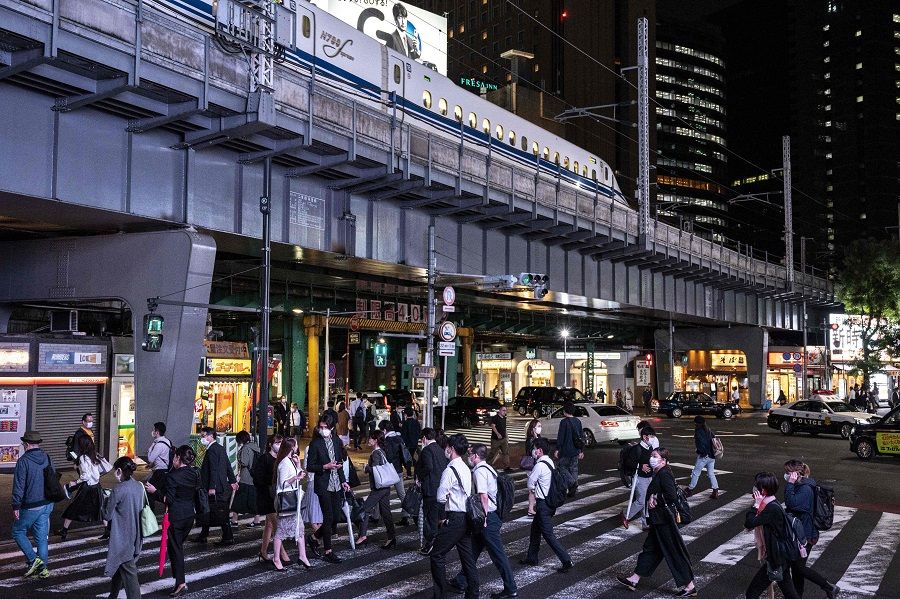 People cross a street while a Shinkansen leaves the city in Tokyo's Shimbashi area on 1 October 2021. (Charly Triballeau/AFP)