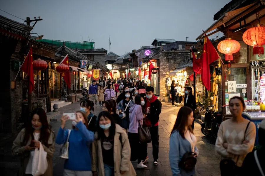 People wearing face masks walk past shops during the country's national "Golden Week" holiday in Beijing on 8 October 2020. (Noel Celis/AFP)