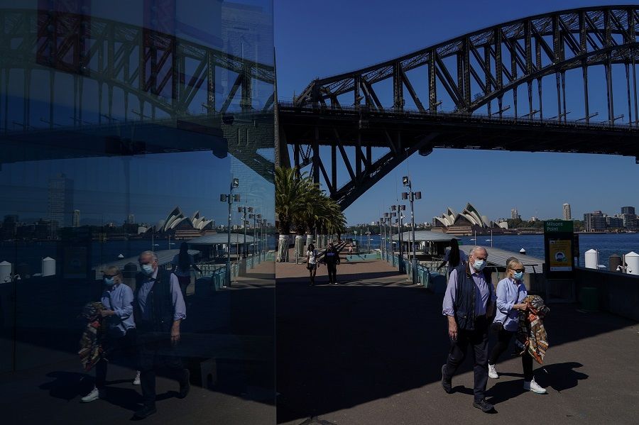 People in protective face masks walk past the Sydney Harbour Bridge in Sydney, Australia, 3 September 2021. (Loren Elliott/Reuters)