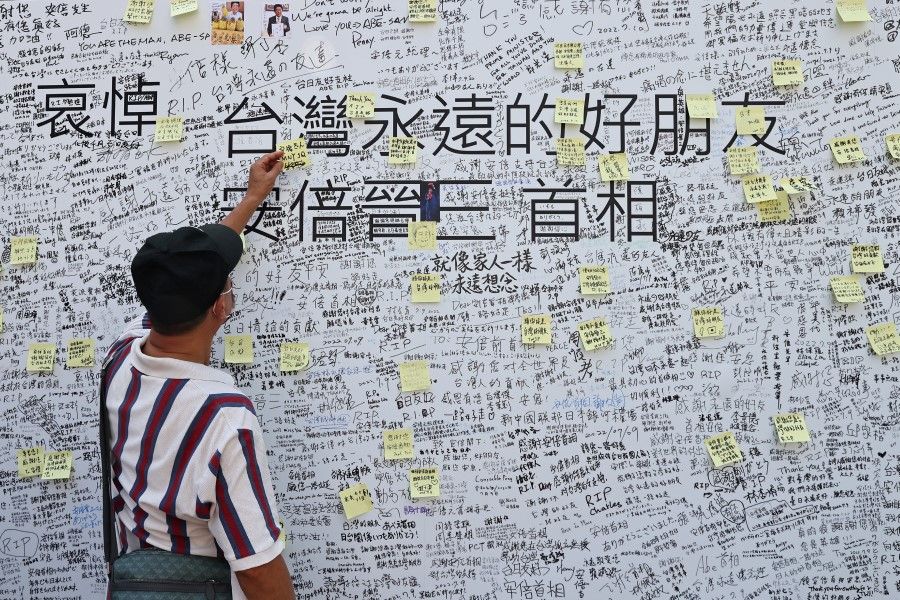 A man leaves a note on a memorial wall for late former Japanese Prime Minister Shinzo Abe, who was shot while campaigning for a parliamentary election, outside of the de-facto Japanese embassy in Taipei, Taiwan, 11 July 2022. (Ann Wang/Reuters)