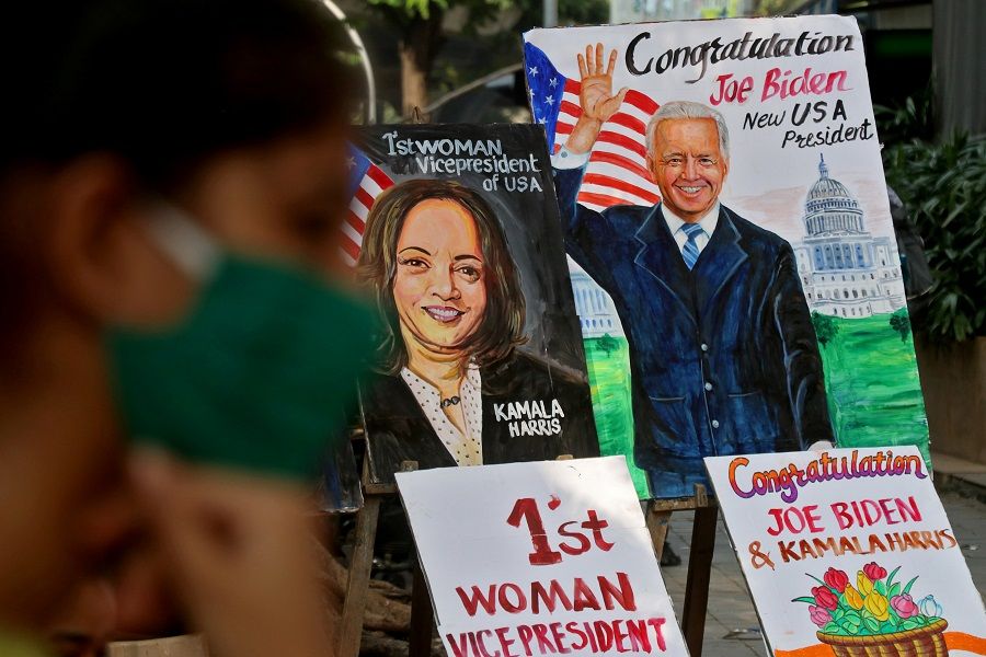 A girl sits next to the paintings of US President-elect Joe Biden and Vice President-elect Kamala Harris on display alongside a road in Mumbai, India, 8 November 2020. (Niharika Kulkarni/Reuters)