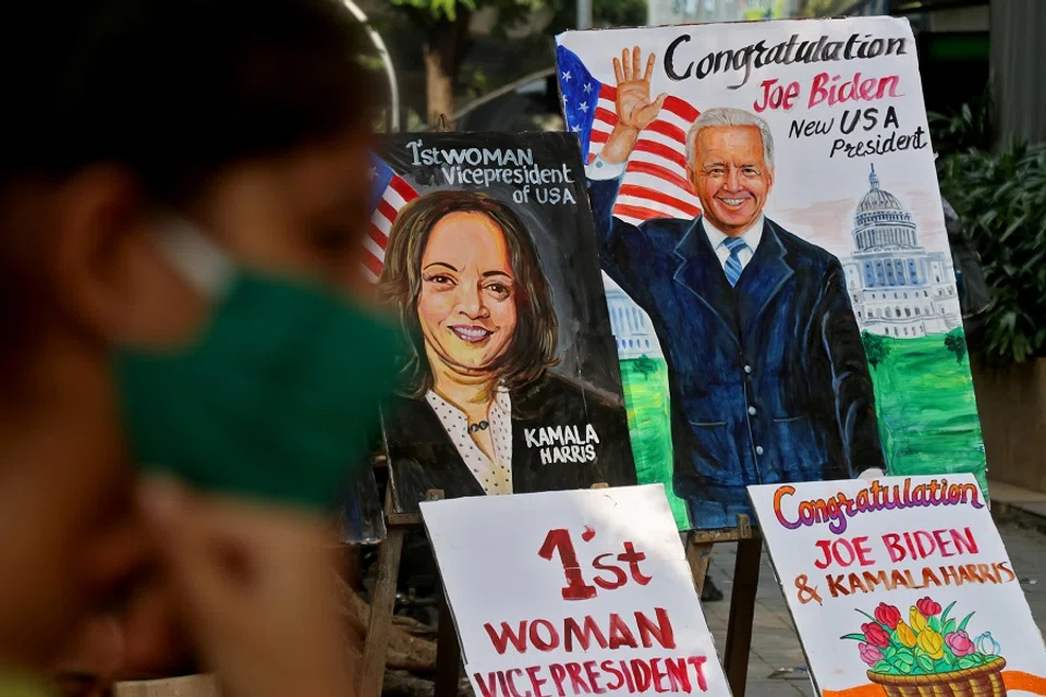 A girl sits next to the paintings of US President-elect Joe Biden and Vice President-elect Kamala Harris on display alongside a road in Mumbai, India, 8 November 2020. (Niharika Kulkarni/Reuters)