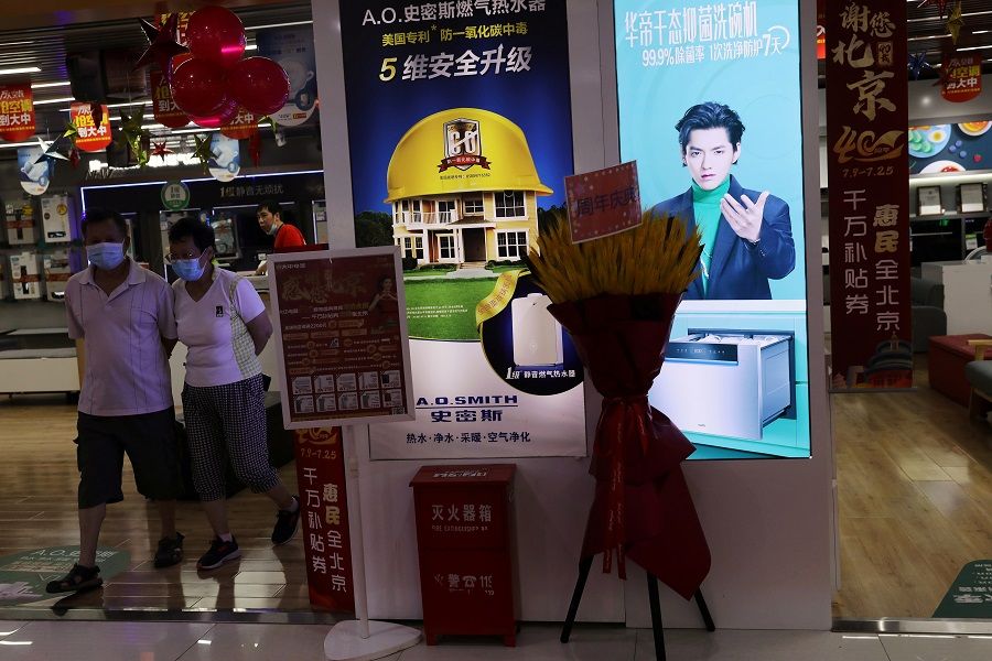 People walk next to a home appliances store displaying an advertisement that features singer-actor Kris Wu, at a shopping mall in Beijing, China, 20 July 2021. (Tingshu Wang/Reuters)