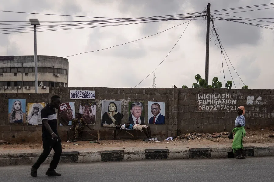 A pedestrian walks next to paintings of the President of Nigeria Bola Tinubu (third left on wall) and US President Donald Trump (second right on wall) displayed in the street in Lagos, on 21 February 2025. (Olympia de Maismont/AFP)
