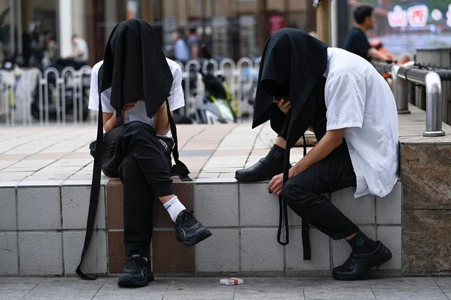 Two store employees sheltering under a cloth use their mobile phone along a road in Beijing on 12 June 2026.