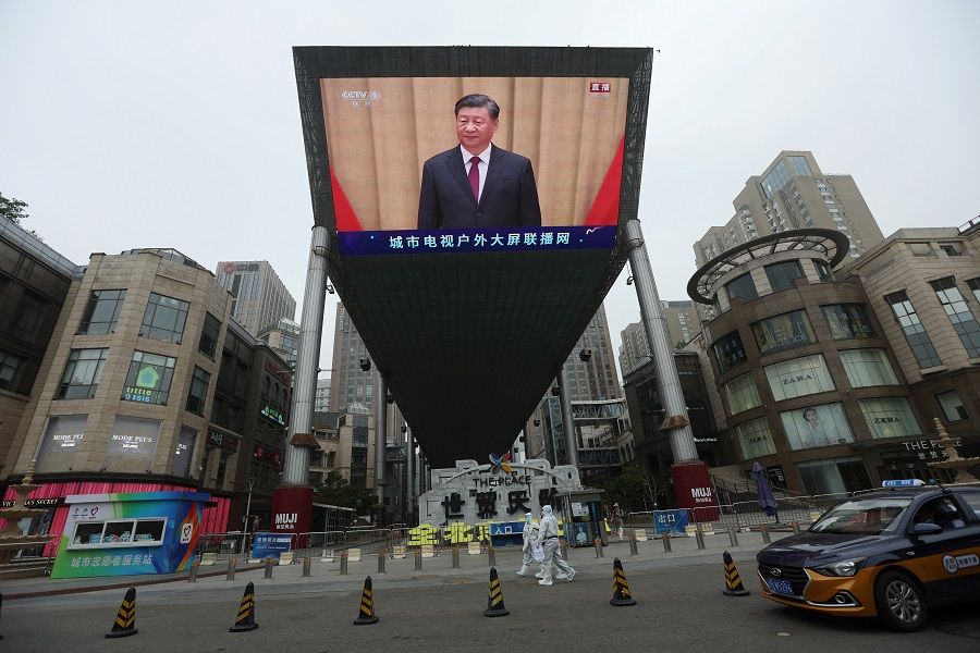 Medical workers in protective suits walk past a giant screen showing Chinese President Xi Jinping at an event celebrating the 100th anniversary of the founding of the Chinese Communist Youth League, amid the Covid-19 outbreak in Beijing, China, 10 May 2022. (Tingshu Wang/Reuters)