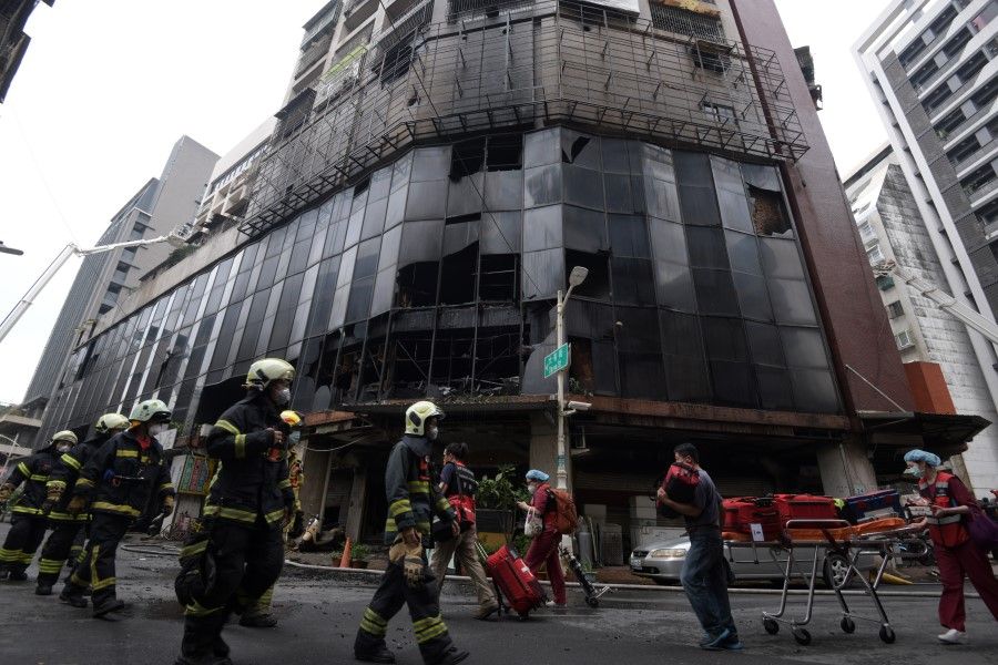 Firefighters and medical workers walk past the damaged Cheng Chung Cheng Building following a fire in Kaohsiung, Taiwan, 14 October 2021. (Woo Swee Kay/Handout via Reuters)