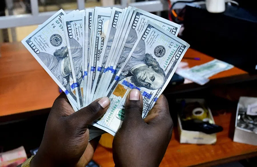 A teller handles US dollar notes inside the cashier's booth at a forex exchange bureau as the dollar rate continues to escalate in Kampala, Uganda, 14 October 2026.