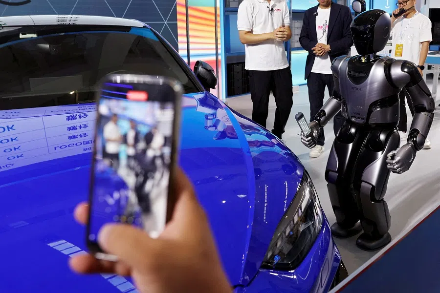 A visitor holds a mobile phone as a UBTECH humanoid robot demonstrates its applications on a factory assembly line, at the World Robot Conference in Beijing, China, on 21 August 2024. (Florence Lo/Reuters)