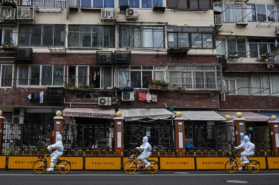 People wearing personal protective equipment cycle on a street during a Covid-19 lockdown in the Jing'an district of Shanghai on 29 May 2022. (Hector Retamal/AFP)