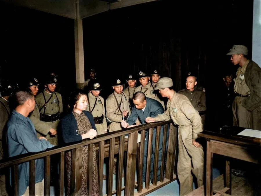 10 June 1950. Four defendants standing before the courtroom railing — (from right to left) Nie Xi, Wu Shi (bowing his head while writing his final testament), Zhu Feng and Chen Baocang — listen to the death sentence being pronounced. They were then tightly bound and escorted to the execution ground.