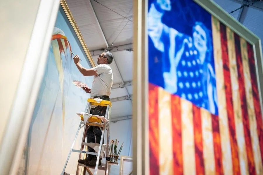 A painter works on an American Flag painting as attendees visit booths representing various US states during the Great American State Fair on the National Mall in Washington, DC, US, on 25 June 2026.