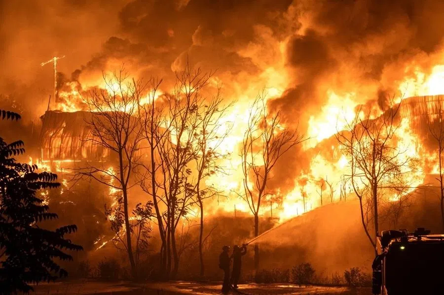 Firefighters try to contain a fire at a warehouse facility during a wild fire near Oraiokastro, on the northwest outskirts of Thessaloniki, on 4 July 2026. Record-breaking heat waves and scant rainfall turned forests and fields into tinderboxes, with forecasters warning that more extreme conditions are on the way.