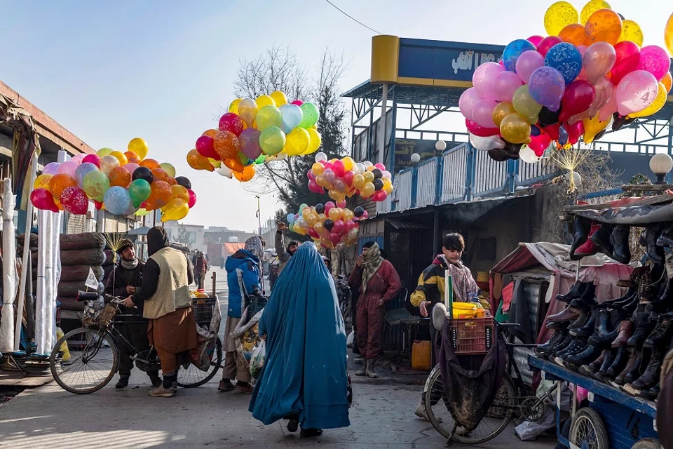 An Afghan burqa-clad woman walks past balloon vendors, at a market in Kabul on 8 January 2025. (Wakil Kohsar/AFP)